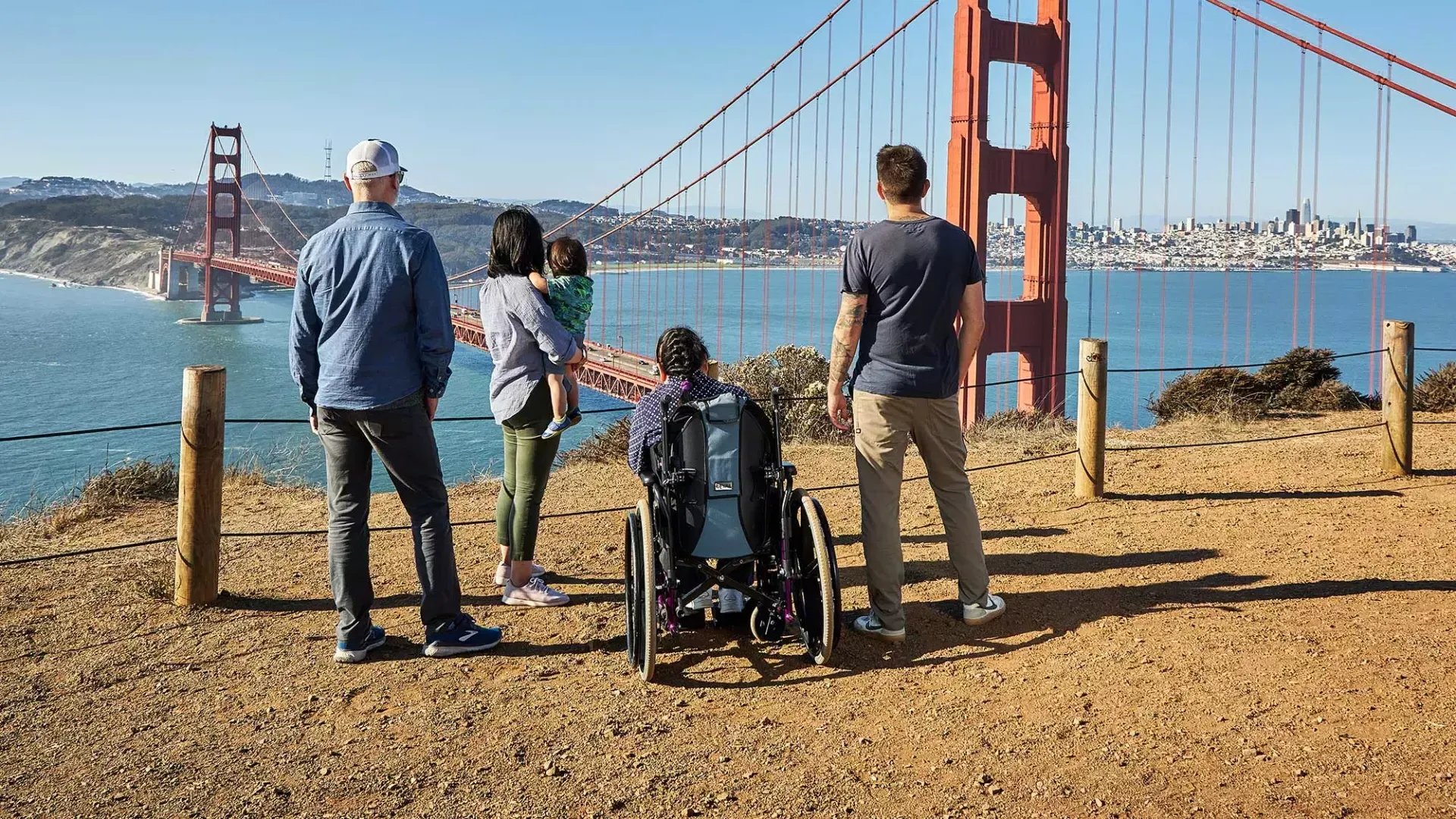Un groupe de personnes, dont une personne en fauteuil roulant, est vu de dos alors qu'ils regardent le Golden Gate Bridge depuis Marin Headlands.
