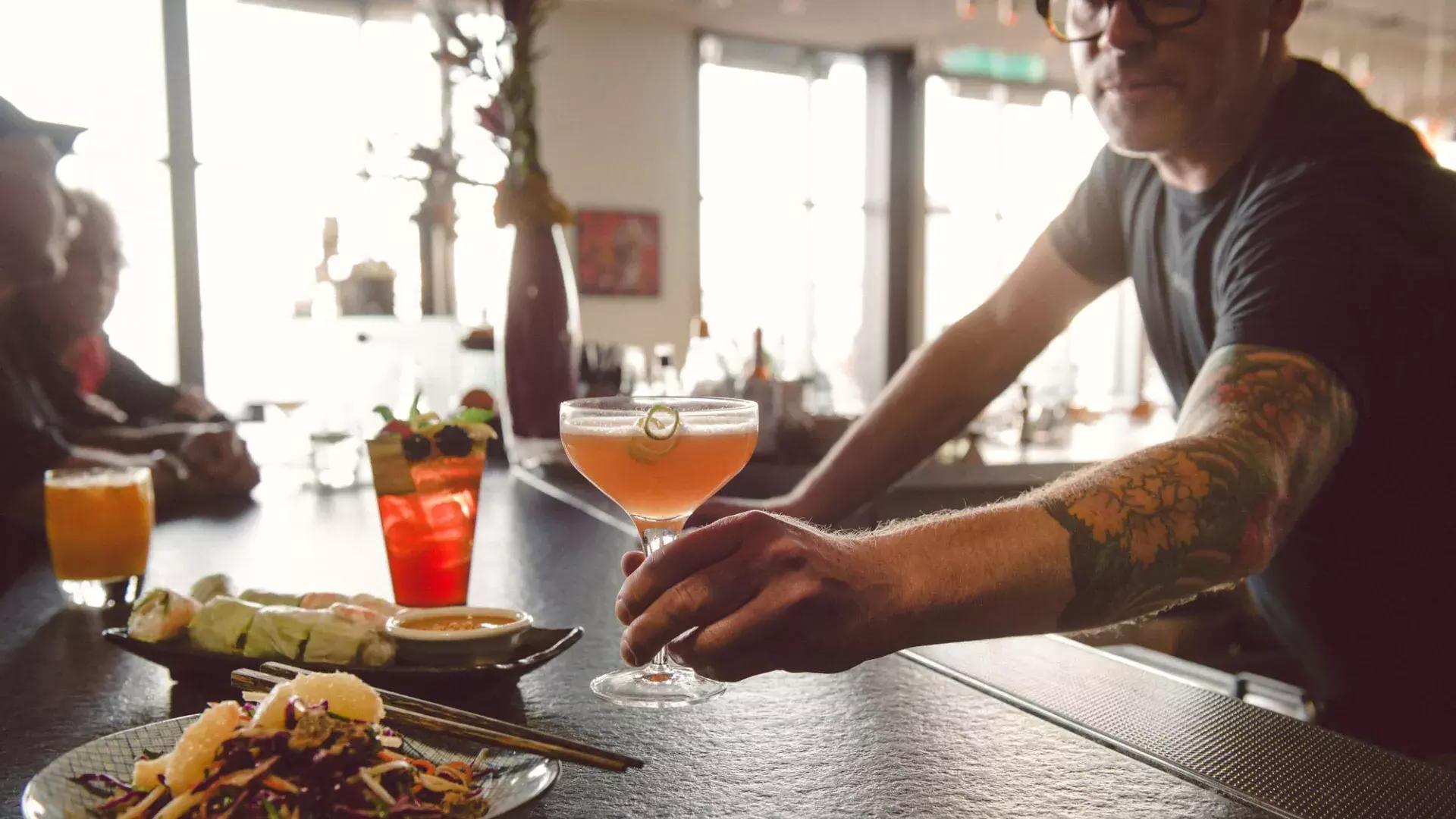 在贝博体彩app的一家酒吧里，一名调酒师为顾客端上鸡尾酒.