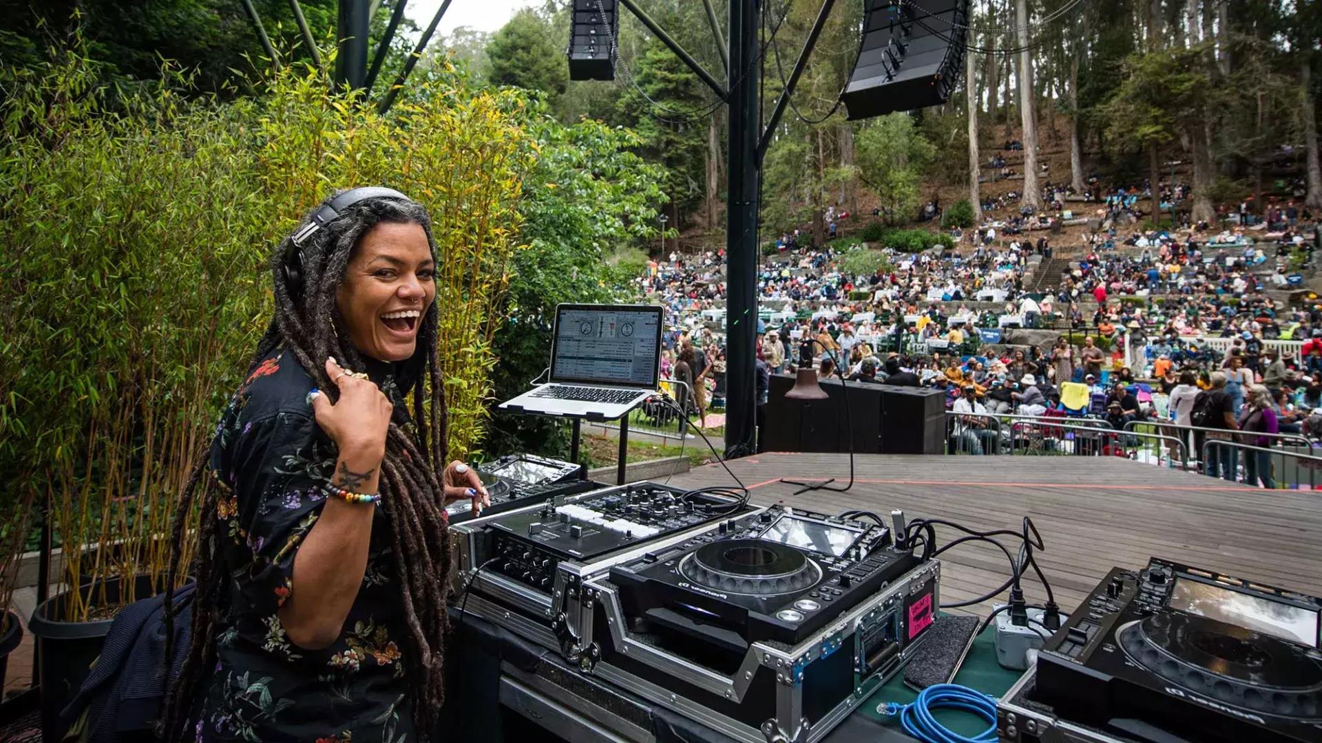 Une femme DJ au Stern Grove Festival regarde par-dessus son épaule et sourit à la caméra.