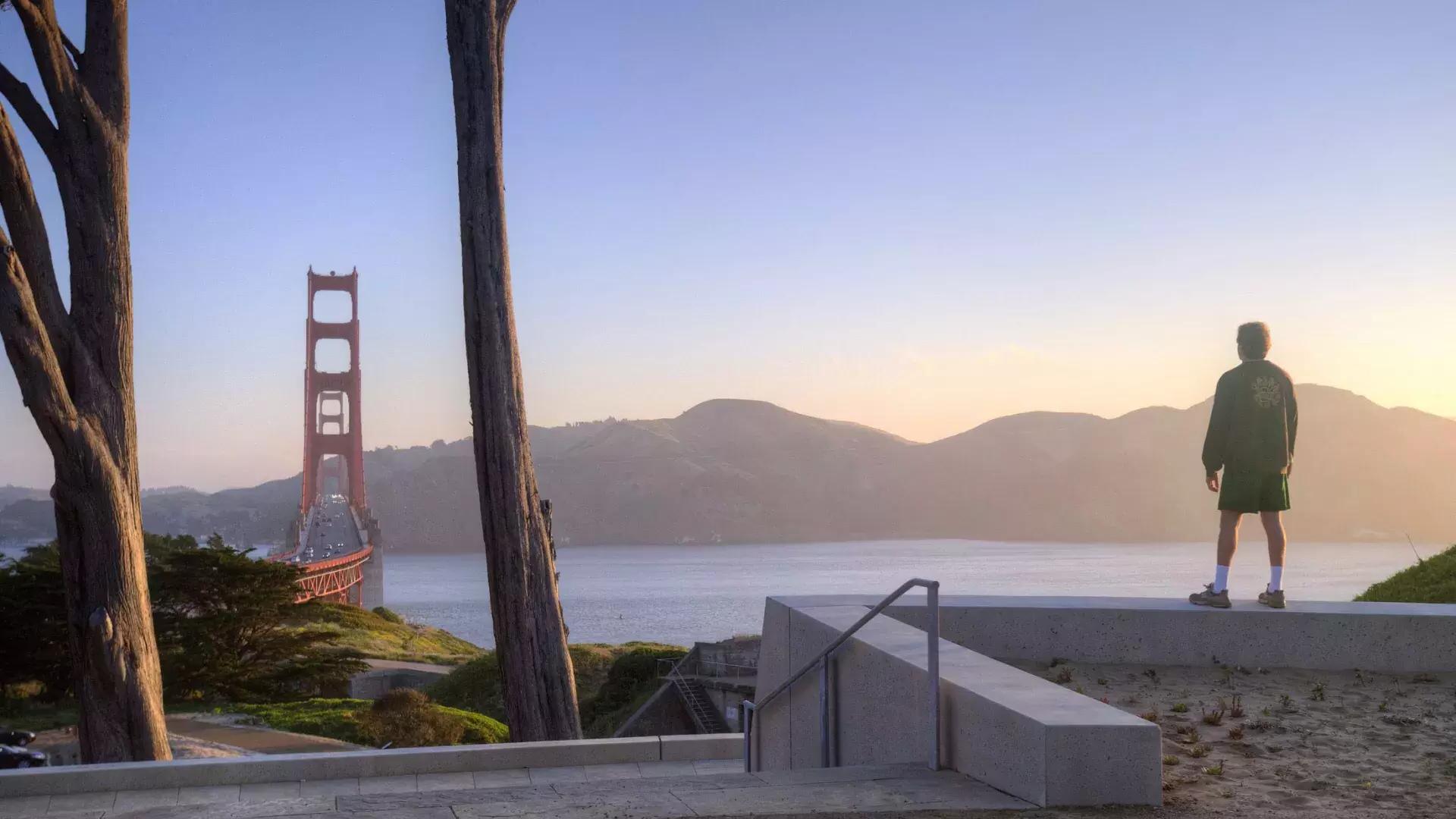 Um homem observa a ponte Golden Gate com montanhas ao fundo.