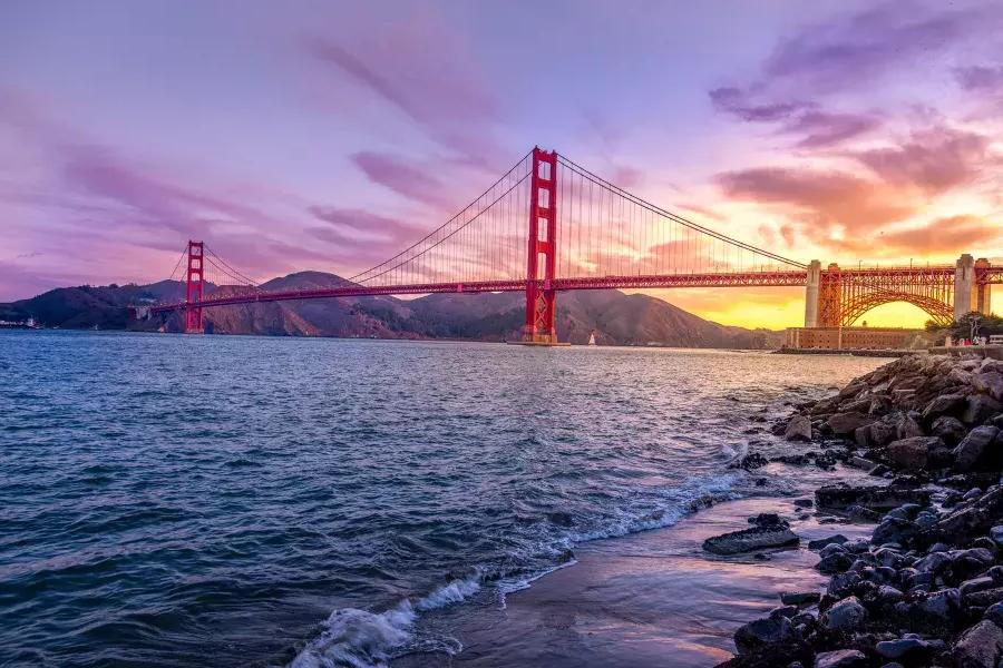 El puente Golden Gate al atardecer con un cielo multicolor y la Bahía de 贝博体彩app en primer plano.