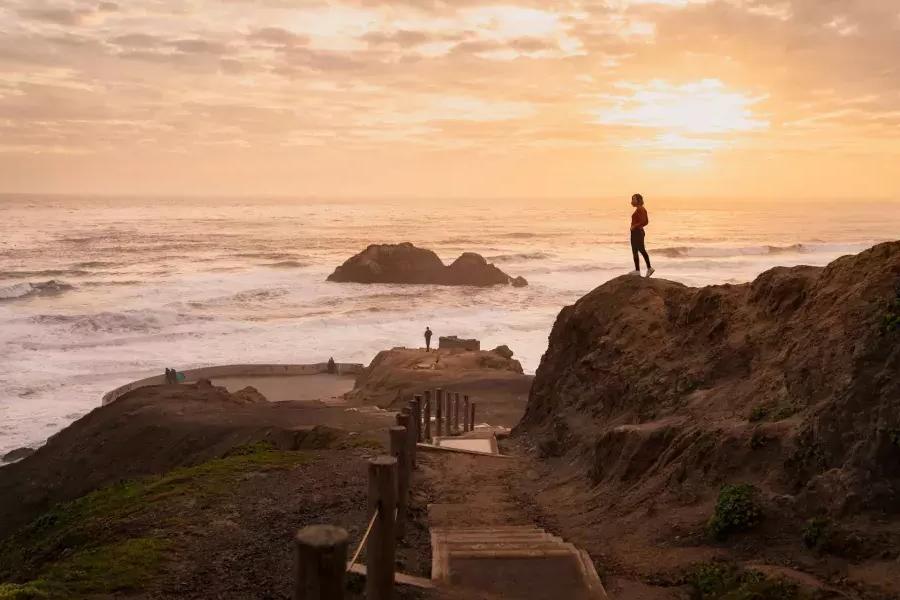 Duas pessoas estão em rochas com vista para o oceano em Sutro Baths, em São Francisco.