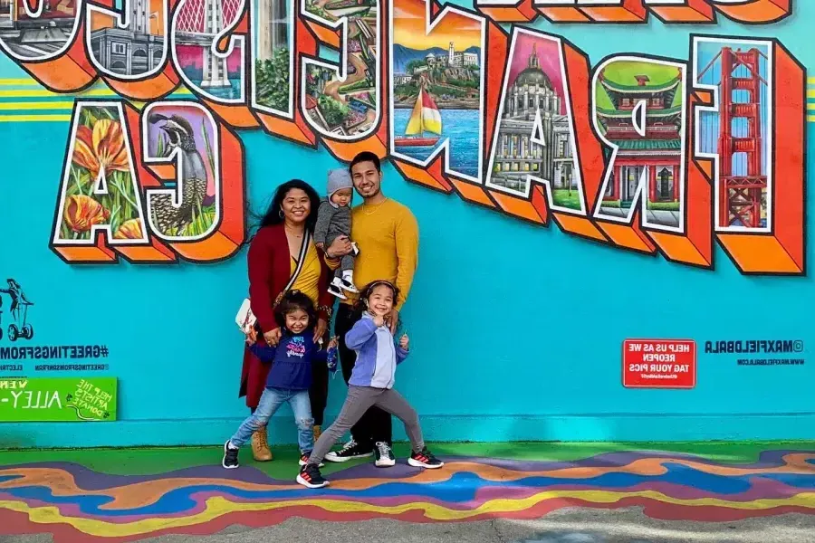 Una familia posando para una foto frente a un mural de San Francisco