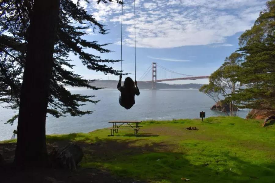 Uma mulher balança em um balanço de árvore com vista para a Ponte Golden Gate. São Francisco, Califórnia.