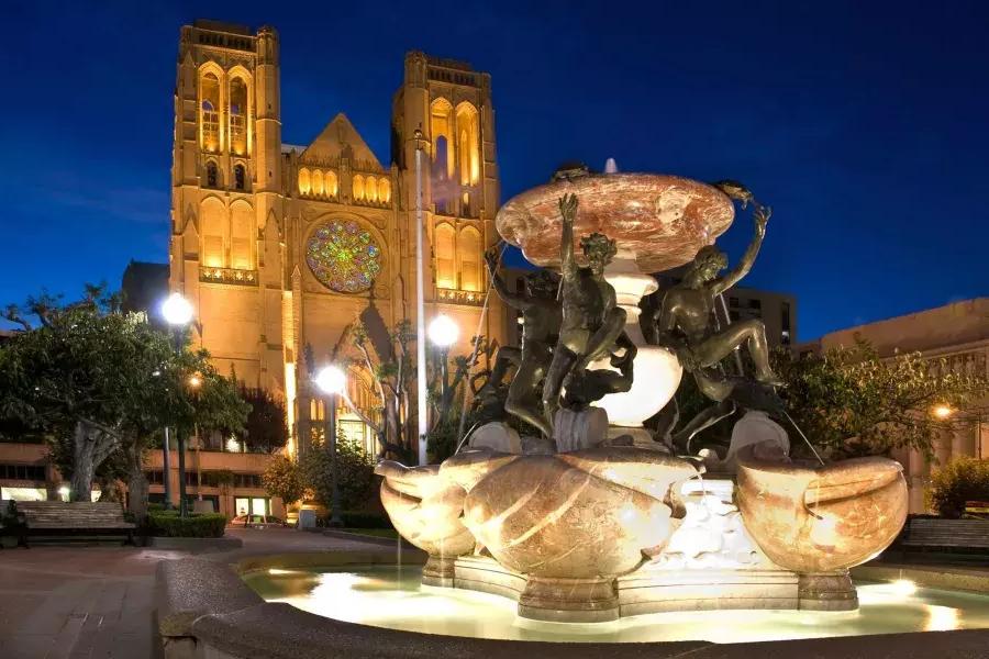Die Grace Cathedral in San Francisco ist bei Nacht abgebildet, mit einem verzierten Springbrunnen im Vordergrund.