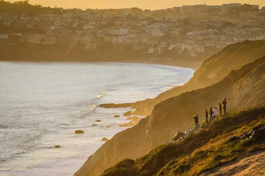 Eine Gruppe von Menschen steht auf einer Klippe am Meer und beobachtet den Sonnenuntergang im Presidio von San Francisco.