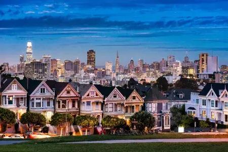 The famous Painted Ladies of Alamo Square are pictured before the San Francisco skyline at twilight.