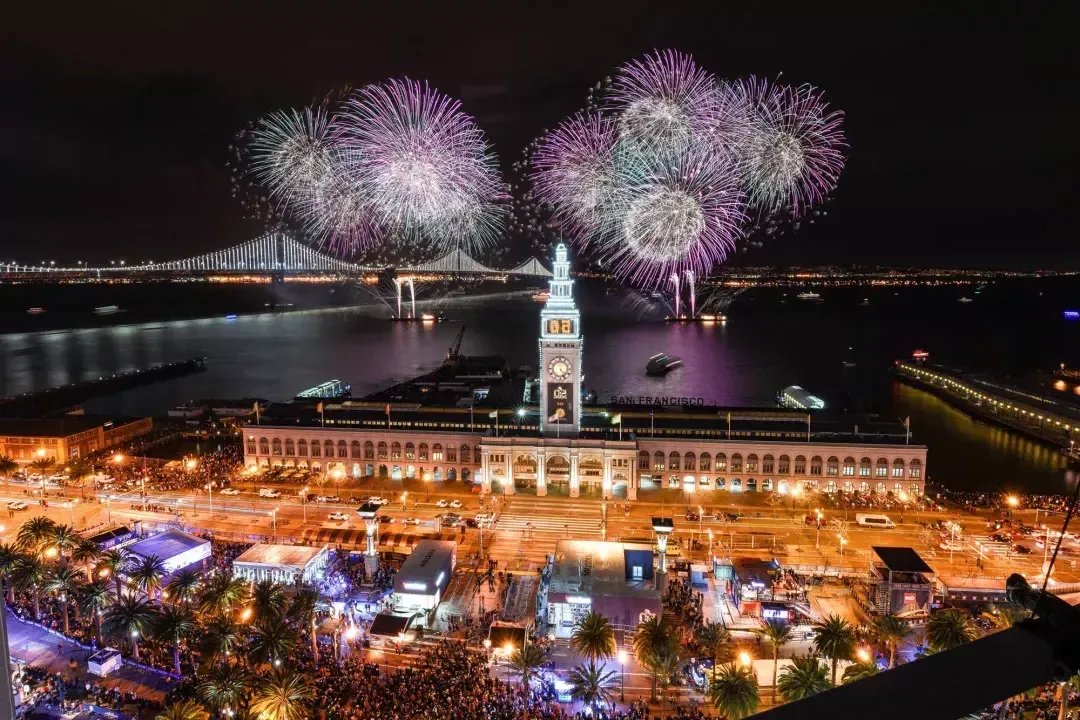 Fireworks explode over top of the Ferry Building, with the Bay Bridge in the background. San Francisco, California.