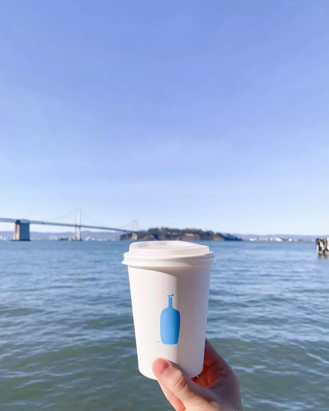 手拿着蓝瓶咖啡杯俯瞰海湾
