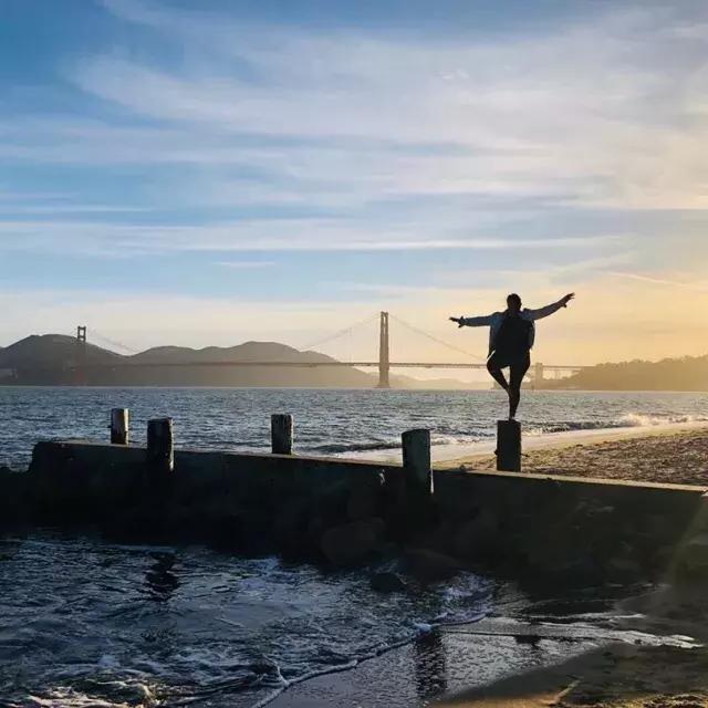 A woman stands on a pier in San Francisco's Marina neighborhood, looking out at the Golden Gate Bridge.