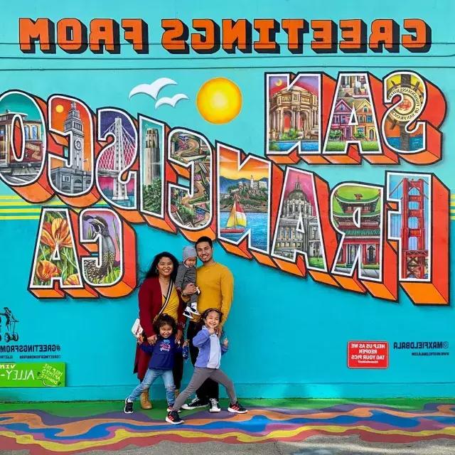 Una famiglia in posa per una foto davanti a un murale di San Francisco