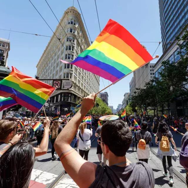 Passanten der San Francisco Pride Parade schwenken Regenbogenfahnen.